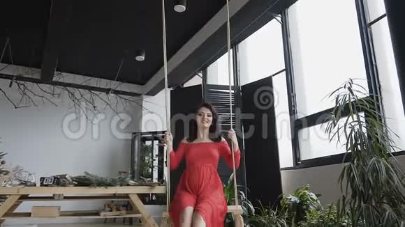 一位年轻漂亮的孕妇穿着一件红色的长裙在一间时髦的大工作室里荡秋千享受着欢乐视频的预览图
