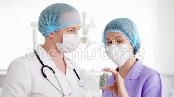 两名戴着医用口罩的女医生在医院讨论新的治疗方法一瓶药丸视频的预览图