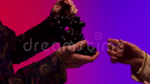 男人把一串又大又黑又多汁的葡萄给老妇人的手在五颜六色的背景下被隔离开来库存快关门视频的预览图