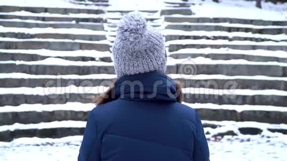 带帽子的女人的后视图停留在一个公园而下雪的楼梯背景孤独的女人独自站着雪雪视频的预览图