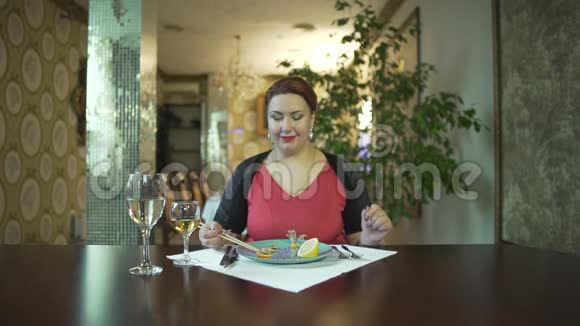 漂亮的微笑着的中年黑发女人穿着红色连衣裙独自一人在高档餐厅吃饭视频的预览图