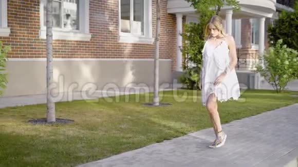 迷人的年轻模特穿着白色连衣裙和运动鞋在街上摆姿势感官上看着镜头视频的预览图