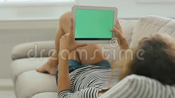 沙发上美丽的少女正在看平板电脑微笑着上网视频的预览图