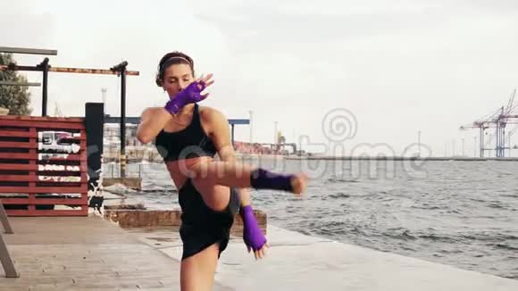 年轻的女拳击手在海边缓慢地练习双腿侧踢漂亮的女拳击手训练视频的预览图