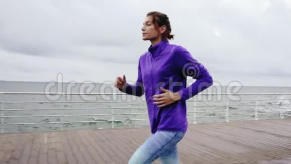近距离观看年轻的运动女子在海边的长廊上慢动作地在户外跑步享受清晨的跑步视频的预览图