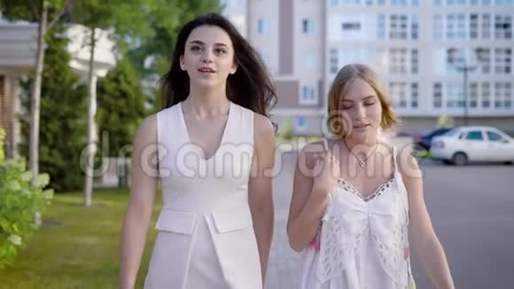 两个穿着白色时尚连衣裙的迷人女孩在夏天的街头背景上谈论着热闹视频的预览图