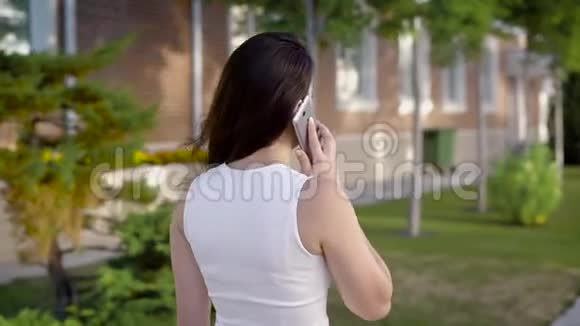 在夏季街头背景下在白色会说话的智能手机上可以看到匿名的深色头发视频的预览图
