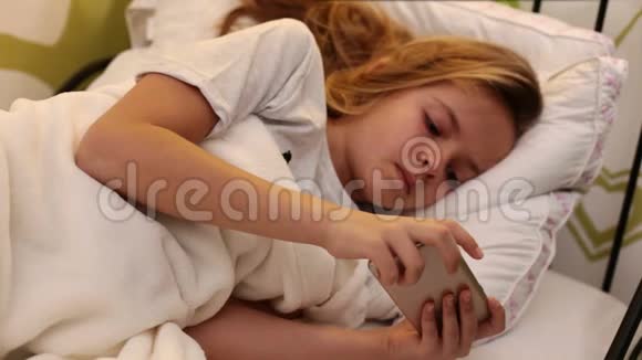年轻的不开心的女孩红着眼睛在床上用智能手机视频的预览图