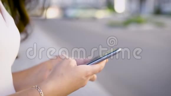 夏季在模糊的街道背景下用智能手机拍摄女性手的作物特写镜头视频的预览图