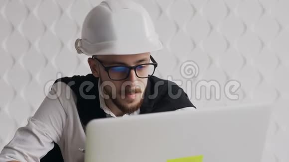 一位年轻建筑师的特写镜头他戴着胡须和眼镜为了自己的安全戴着一个白头盔并在一个视频的预览图