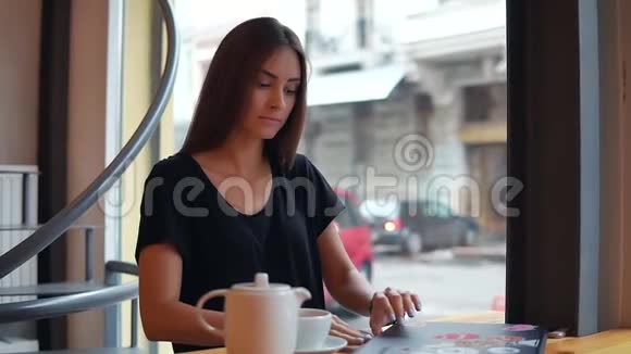 年轻女子坐在咖啡店里喝咖啡休息她打开笔记本电脑开始工作和冲浪视频的预览图