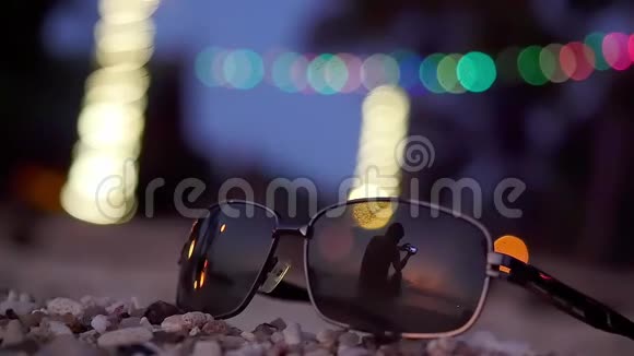 太阳镜躺在热带海滩上年轻人使用手机的剪影反映在背景上视频的预览图