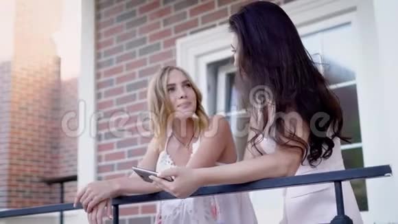 时尚的年轻女孩分享智能手机同时在砖房的阳台上摆姿势视频的预览图