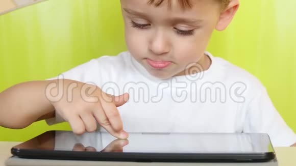 坐在桌子旁的孩子触摸平板电脑的电子显示器一个孩子在玩手提电脑视频的预览图