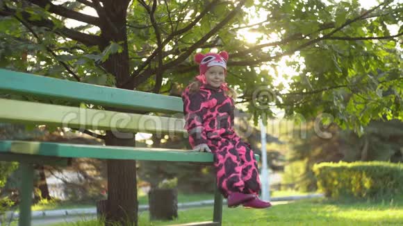 一个可爱的小快乐女孩坐在长凳上双腿在橡树下摆动视频的预览图