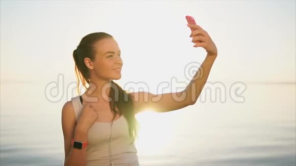年轻快乐的微笑着的女人在海边用智能手机自拍视频的预览图