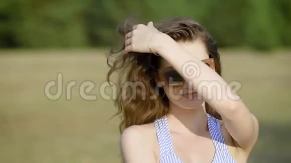 一幅年轻的休闲女性戴着太阳镜在乡村田野的镜头前安详地摆姿势的照片视频的预览图