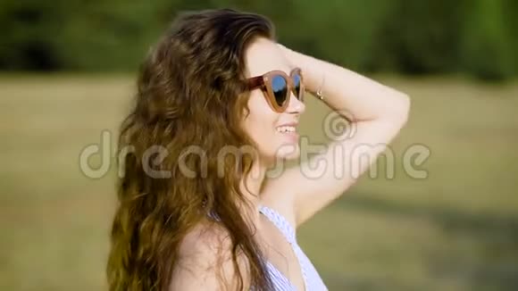 戴着太阳镜在阳光下高高兴兴地在大自然上摆姿势的年轻女子视频的预览图