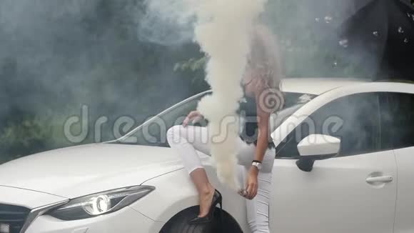 站在白色汽车旁的漂亮的金发女郎漂亮的女孩用烟摆姿势慢动作视频的预览图