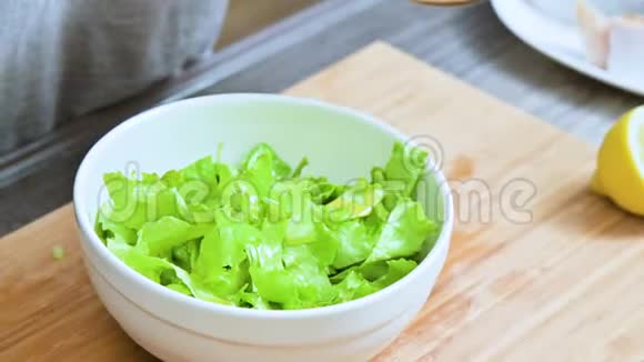 家庭厨房中的女性手的特写被添加到素叶沙拉酱中并在木制的勺子上混合视频的预览图