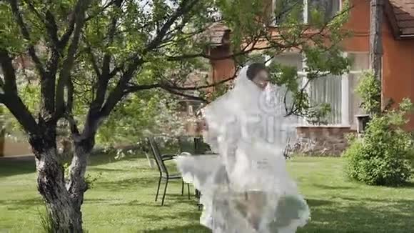美丽的新娘穿着一件白色连衣裙有一条长长的花边在阳光明媚的日子里早上围着她转微笑着散步视频的预览图