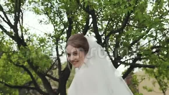 新娘的特写模特她对着镜头微笑穿着一件白色的长花边连衣裙年轻女孩绿色行走视频的预览图