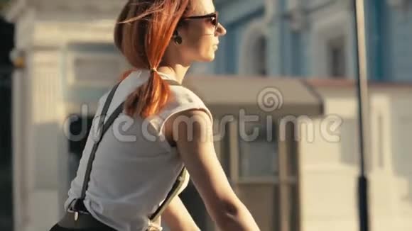 红发妇女骑自行车在城市道路背景建筑慢动作视频的预览图
