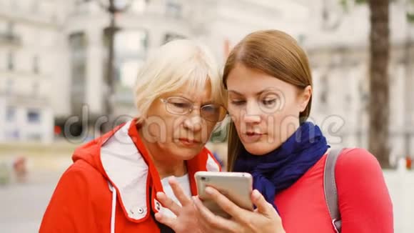 年长的母亲和她的小女儿站在街上使用智能手机幸福的家庭视频的预览图