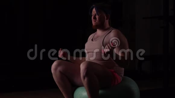 一个穿粉色衣服的超重胖子在健身房里用哑铃和健身球健身视频的预览图