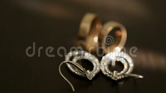 近景黄金结婚戒指和银色新娘耳环与钻石在桌子上视频的预览图