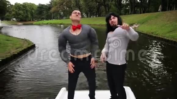 两个穿着假肌肉胸前和双臂垫服装的帅哥在船上唱歌视频的预览图
