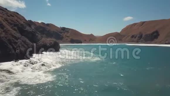 一个阳光明媚的日子在海湾两岸的群山中海浪拍打着岩石海岸视频的预览图