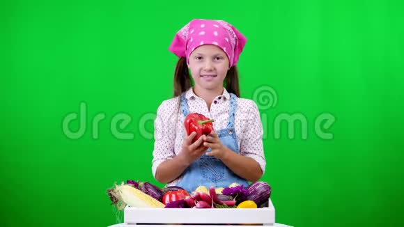 可爱微笑小农家姑娘出示一盒不同新鲜蔬菜收获在工作室的绿色背景上视频的预览图