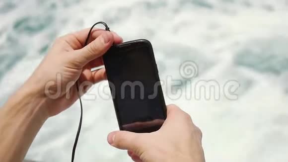 近人手用智能手机听音乐带耳机在海波水蓝背景慢慢慢慢视频的预览图
