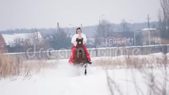 冬天穿着红衣服的黑发年轻女子骑着马在雪地里疾驰视频的预览图