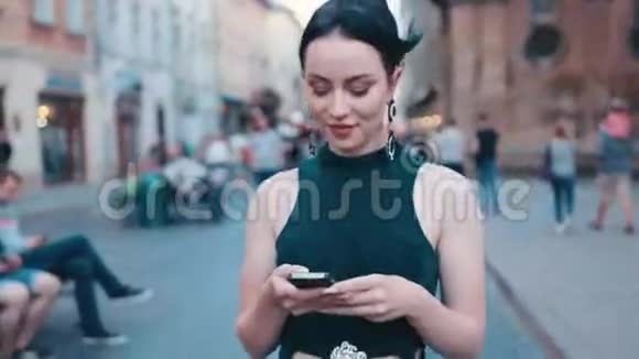 自信漂亮蓝眼睛深褐色头发的女人穿着时尚的服装走在市中心的一条街上用她手机视频的预览图