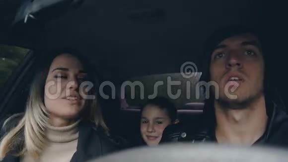年轻幸福的家庭坐车旅行丈夫亲吻妻子坐后座的男孩视频的预览图