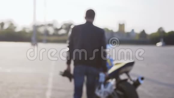 一个穿着黑色皮夹克和蓝色牛仔裤手里拿着头盔的年轻骑摩托车的人视频的预览图