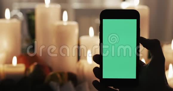 男性手拿着绿色屏幕的智能手机在背景中点燃蜡烛视频的预览图