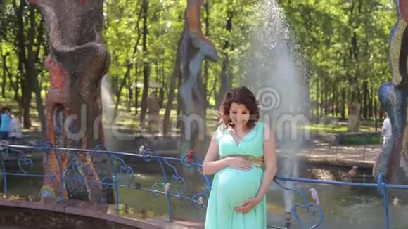在喷泉附近穿裙子的怀孕少女的肖像视频的预览图