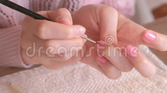 女人用小刷子把第二层粉红色的紫胶涂在指甲上特写双手视频的预览图
