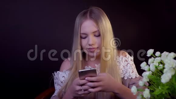 年轻的金发女郎在黑色的背景上微笑它在智能手机上打印一条短信视频的预览图