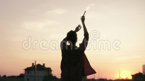 年轻的女人在日落时拿着烟火蜡烛站着看着镜头镜头耀斑慢镜头视频的预览图
