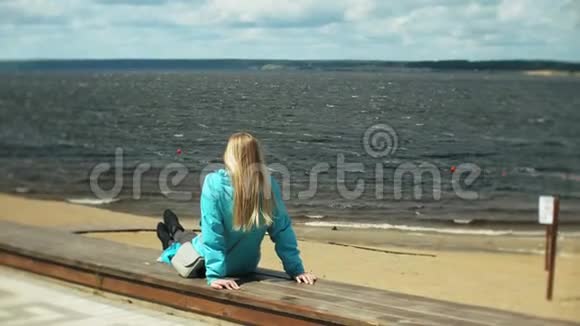 年轻的漂亮女人坐在海边的木墩上看着这座城市可爱的时髦女郎带着背包视频的预览图