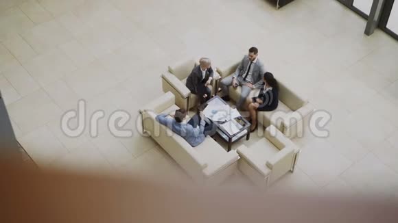一群商业人士同事在现代大厅里坐在沙发上讨论金融图表的最高看法视频的预览图