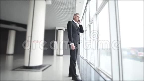 这位老商人在全景窗户附近打电话一个人在手机上说话表情严肃视频的预览图