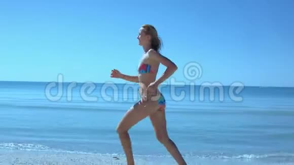 美丽苗条的比基尼女郎沿着海边的海滩奔跑头发随风飘扬奔跑视频的预览图