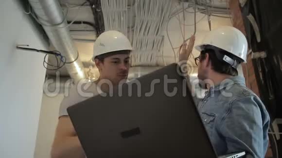 两个戴着头盔的建筑师在谈论着站在建筑工地上的笔记本电脑专家手提电脑视频的预览图