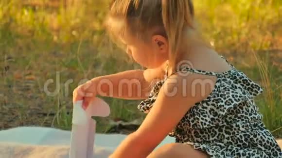 小女孩坐在公园的毯子上从盒子里拿硬币视频的预览图