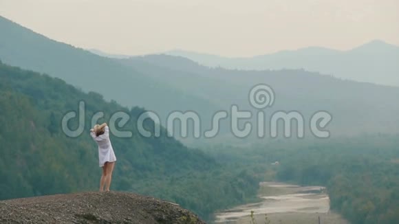 美丽的金发游客正在旋转一边在山边跳舞一边欣赏风景视频的预览图